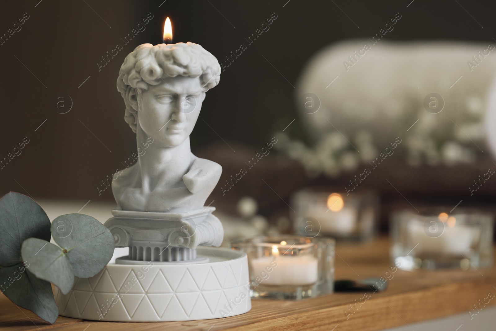 Photo of Beautiful David bust candle and eucalyptus branch on wooden table in room, space for text