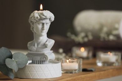 Photo of Beautiful David bust candle and eucalyptus branch on wooden table in room, space for text