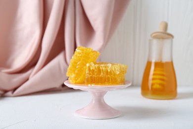 Photo of Stand with natural honeycombs and honey on white table, selective focus. Space for text
