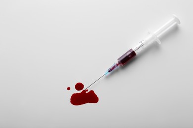 Plastic syringe with blood on white background, top view