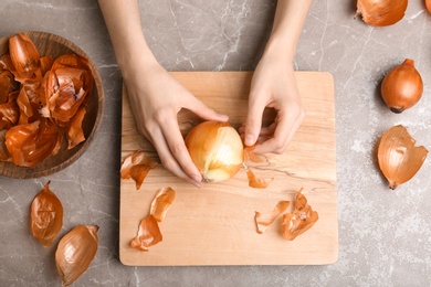 Woman peeling onion at table, top view