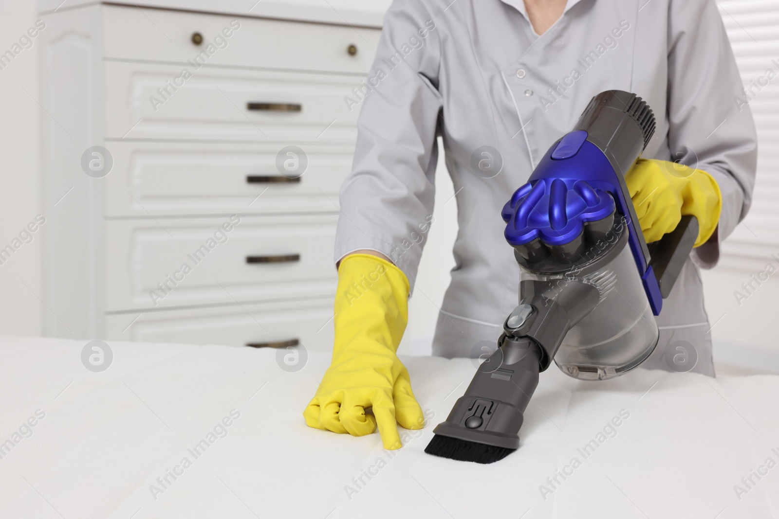 Photo of Woman in gloves disinfecting mattress with vacuum cleaner indoors, closeup. Space for text