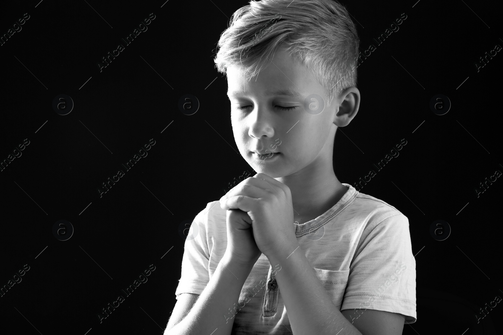 Photo of Little boy with hands clasped together for prayer on dark background, black and white effect. Space for text