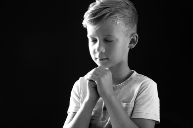 Photo of Little boy with hands clasped together for prayer on dark background, black and white effect. Space for text