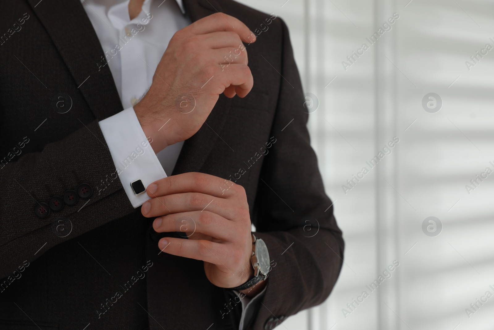 Photo of Man wearing stylish suit and cufflinks near white wall, closeup. Space for text