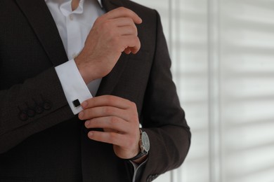 Man wearing stylish suit and cufflinks near white wall, closeup. Space for text