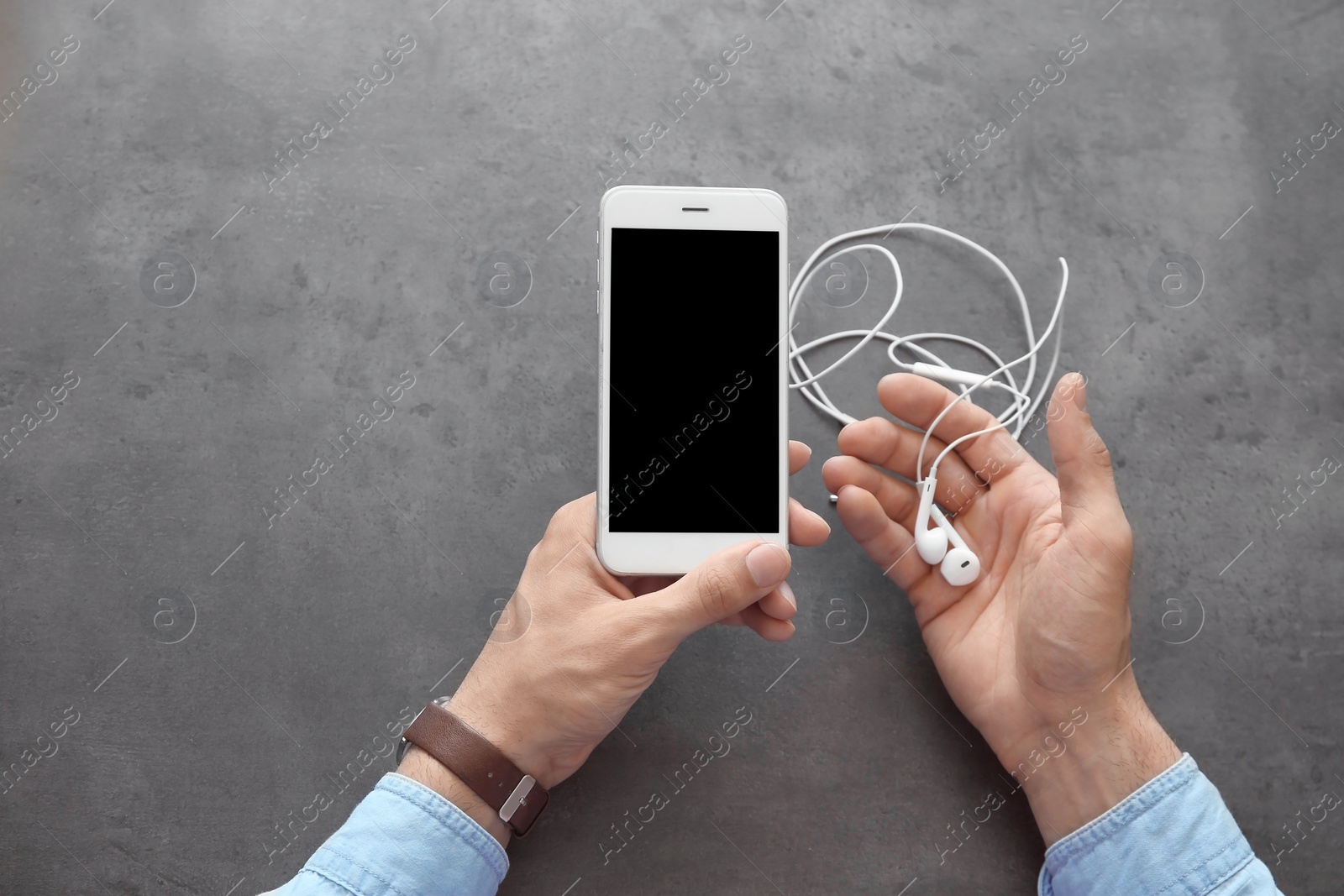 Photo of Young man holding mobile phone with blank screen and earphones in hands over table