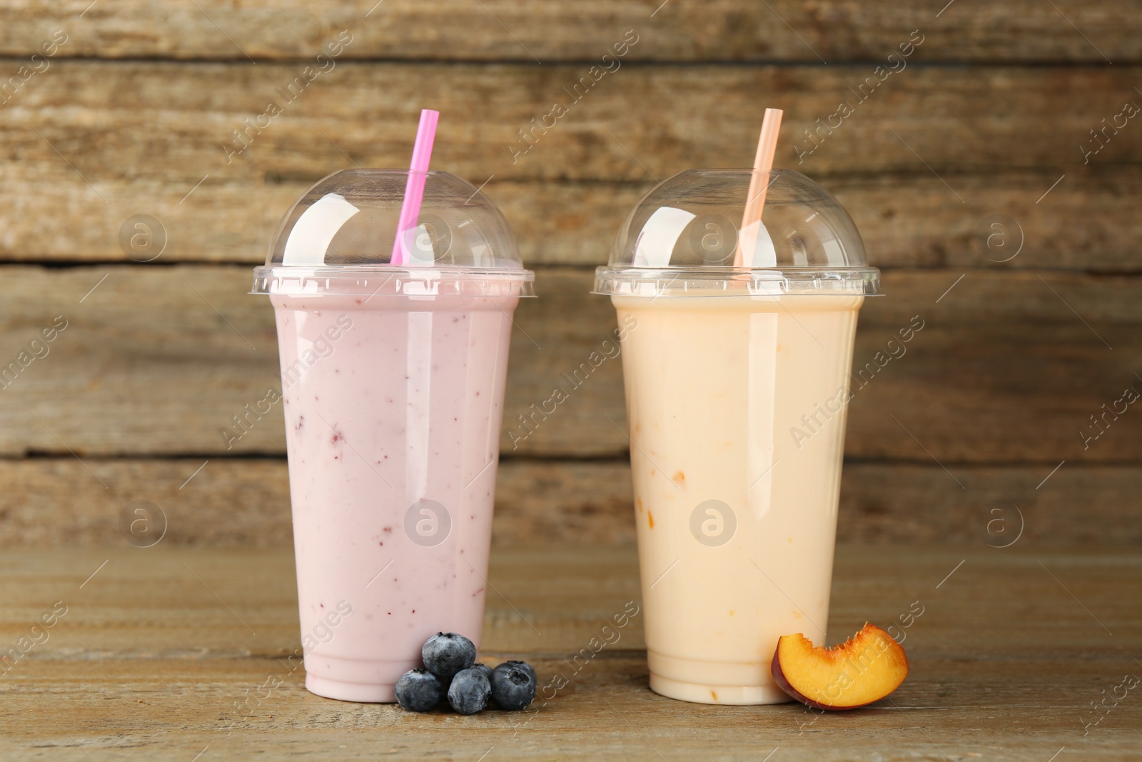 Photo of Plastic cups with different tasty smoothies and fresh fruits on wooden table