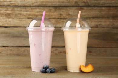 Plastic cups with different tasty smoothies and fresh fruits on wooden table