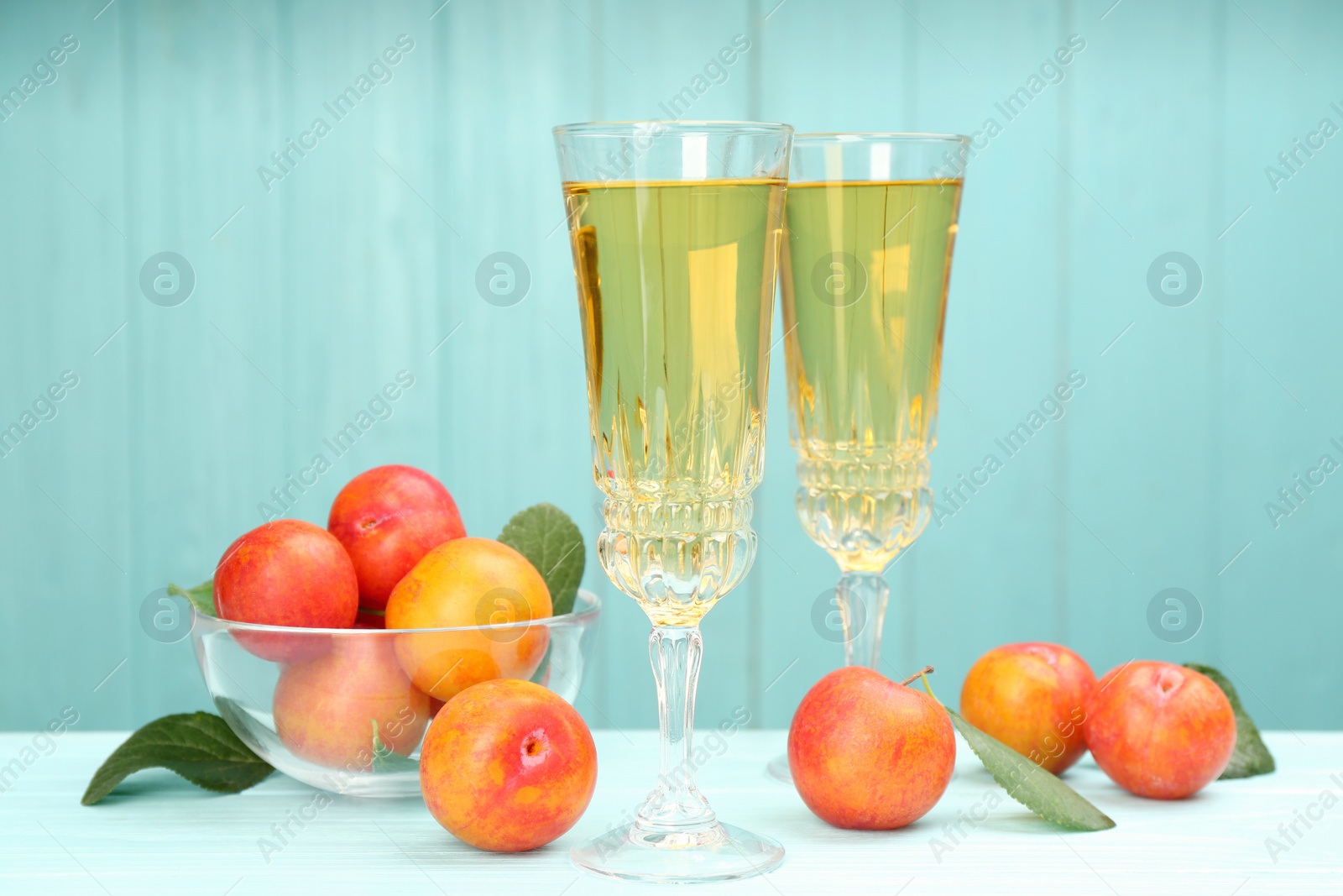 Photo of Delicious plum liquor and ripe fruits on table against light blue background. Homemade strong alcoholic beverage