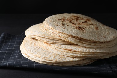 Photo of Many tasty homemade tortillas on black wooden table, closeup