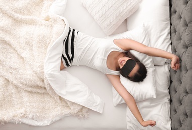 Photo of Young beautiful woman with sleeping mask stretching in bed at home, top view