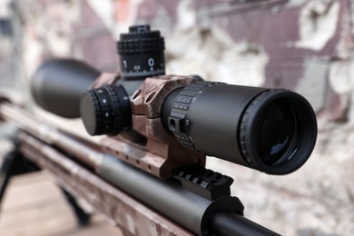 Photo of Closeup view of modern powerful sniper rifle with telescopic sight on blurred background