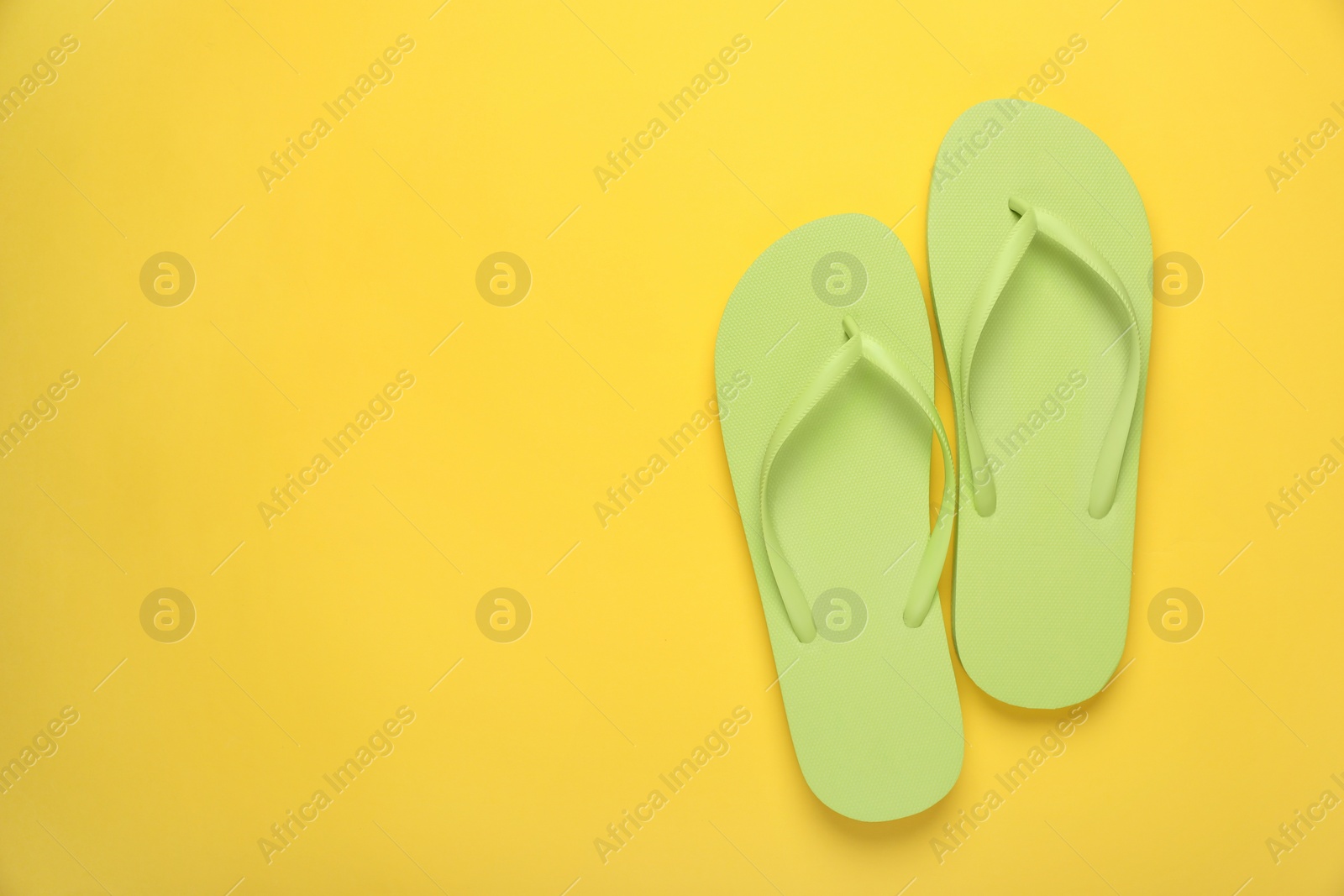 Photo of Stylish light green flip flops on yellow background, top view. Space for text