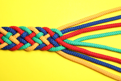 Photo of Braided colorful ropes on yellow background, top view. Unity concept