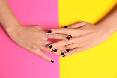 Photo of Woman showing manicure with black nail polish on color background, top view