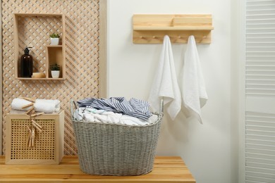 Photo of Wicker basket with dirty laundry on wooden table in bathroom