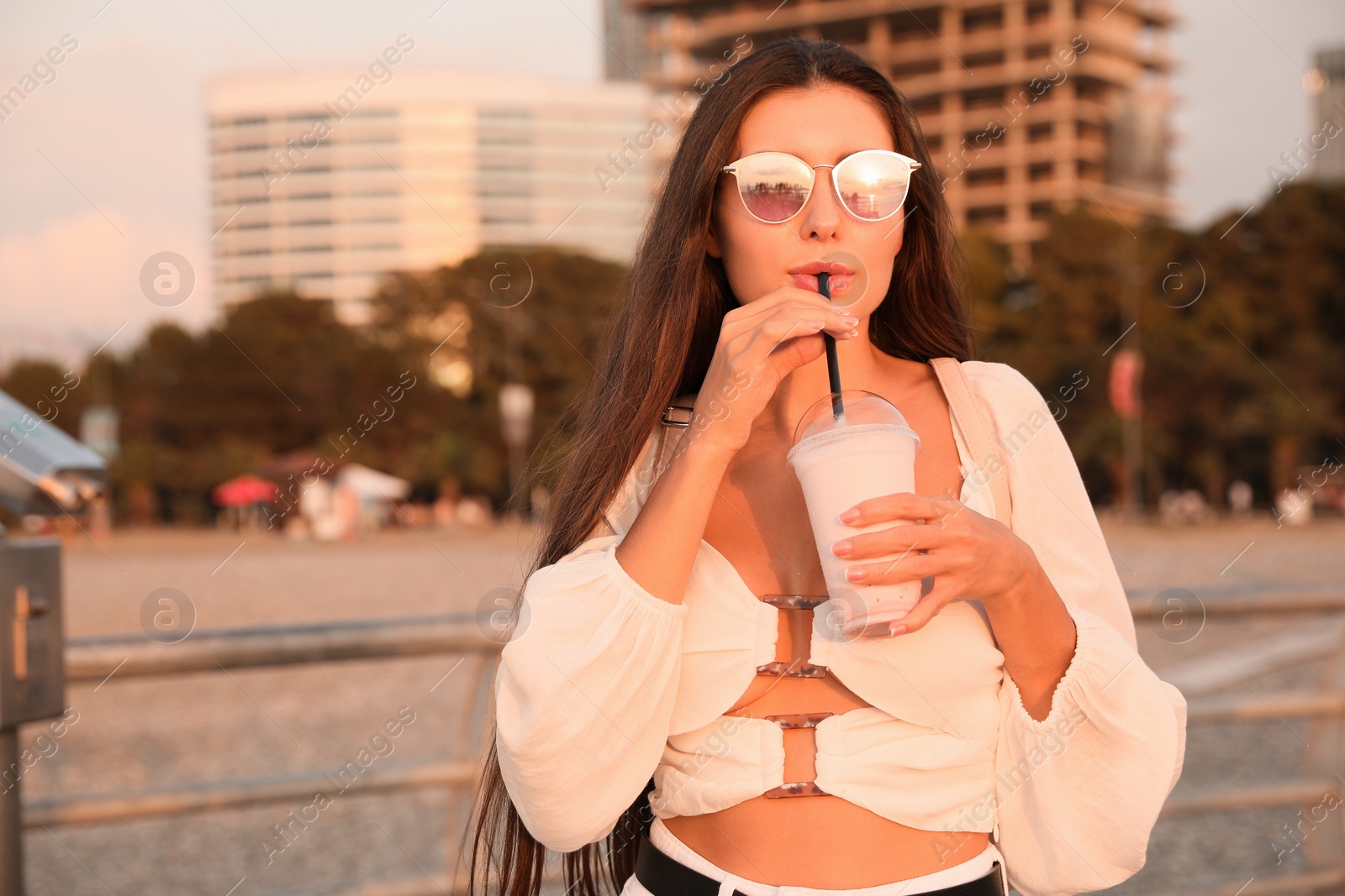 Photo of Beautiful young woman with tasty milk shake outdoors, space for text