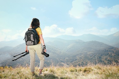 Photo of Professional photographer with modern camera and tripod in mountains, back view. Space for text