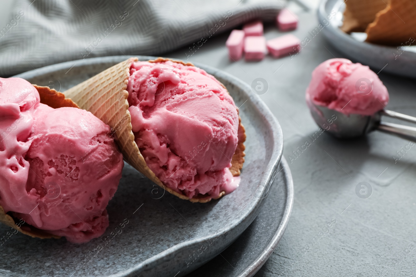 Photo of Delicious pink ice cream in wafer cones served on grey table, closeup