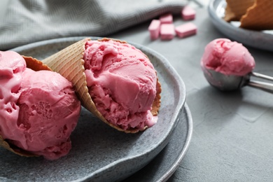 Photo of Delicious pink ice cream in wafer cones served on grey table, closeup