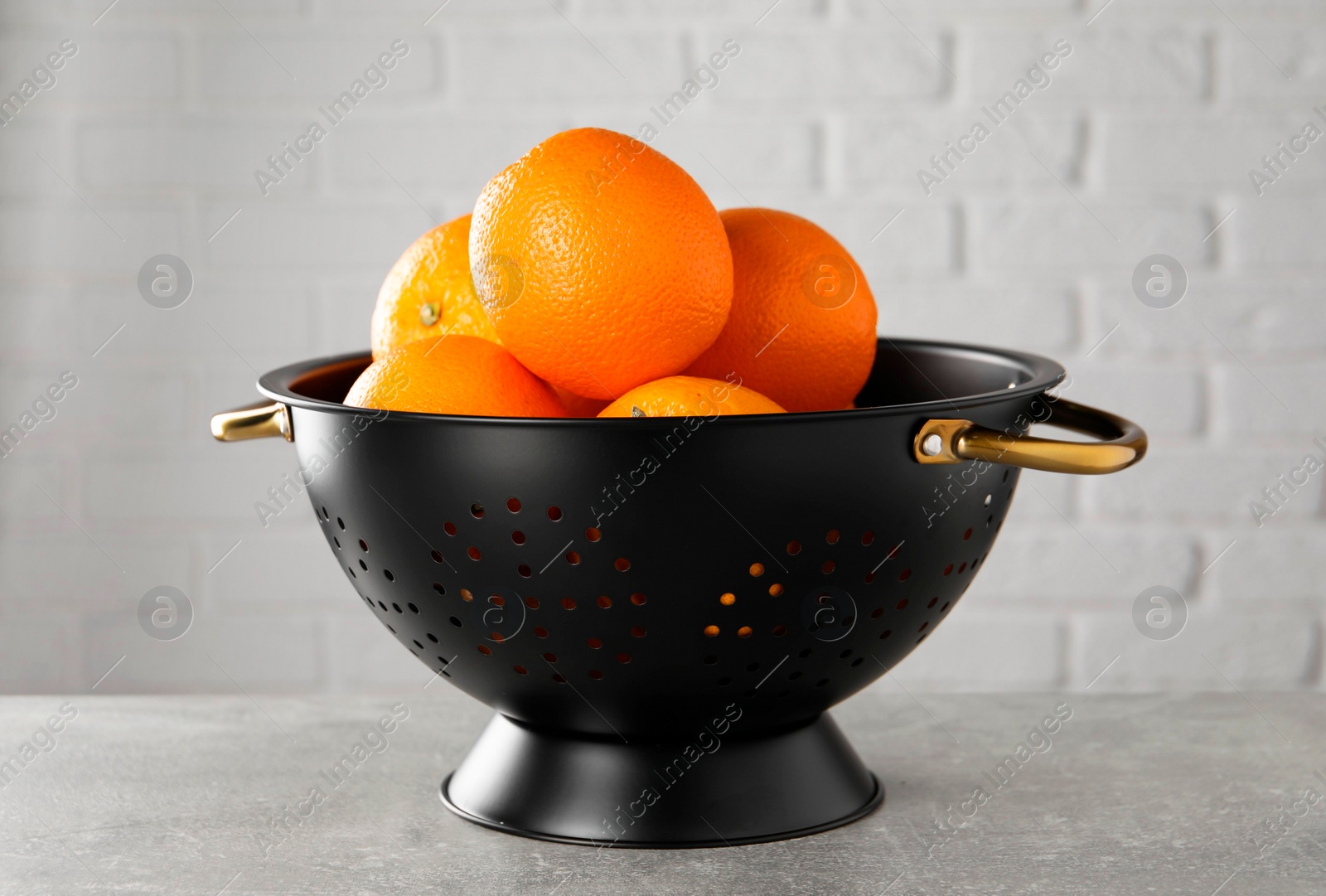 Photo of Fresh ripe oranges in black colander on light grey table