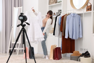 Photo of Smiling fashion blogger showing her clothes while recording video at home