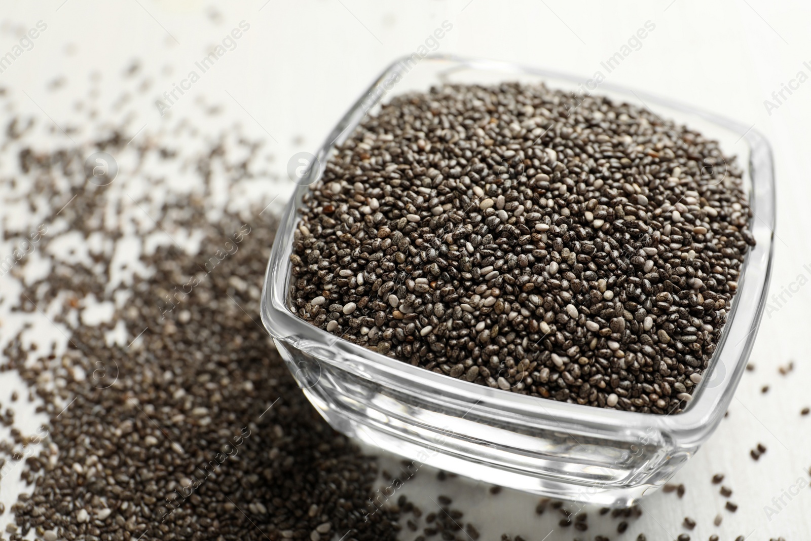 Photo of Glass bowl with chia seeds on white table, closeup