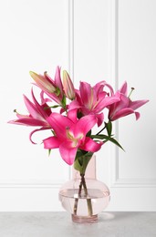 Photo of Beautiful pink lily flowers in vase on light grey table against white wall