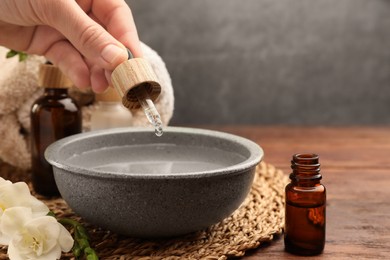 Photo of Woman dripping essential oil into bowl at wooden table, closeup. Aromatherapy treatment