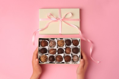 Photo of Child with box of delicious chocolate candies on pink background, top view