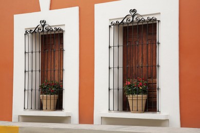 Photo of Orange building with wooden windows and potted plants on windowsills outdoors