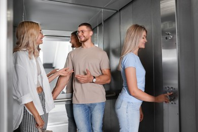 Photo of Happy friends talking while woman choosing floor in elevator
