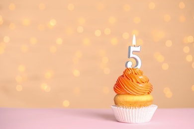Photo of Birthday cupcake with number five candle on table against festive lights, space for text