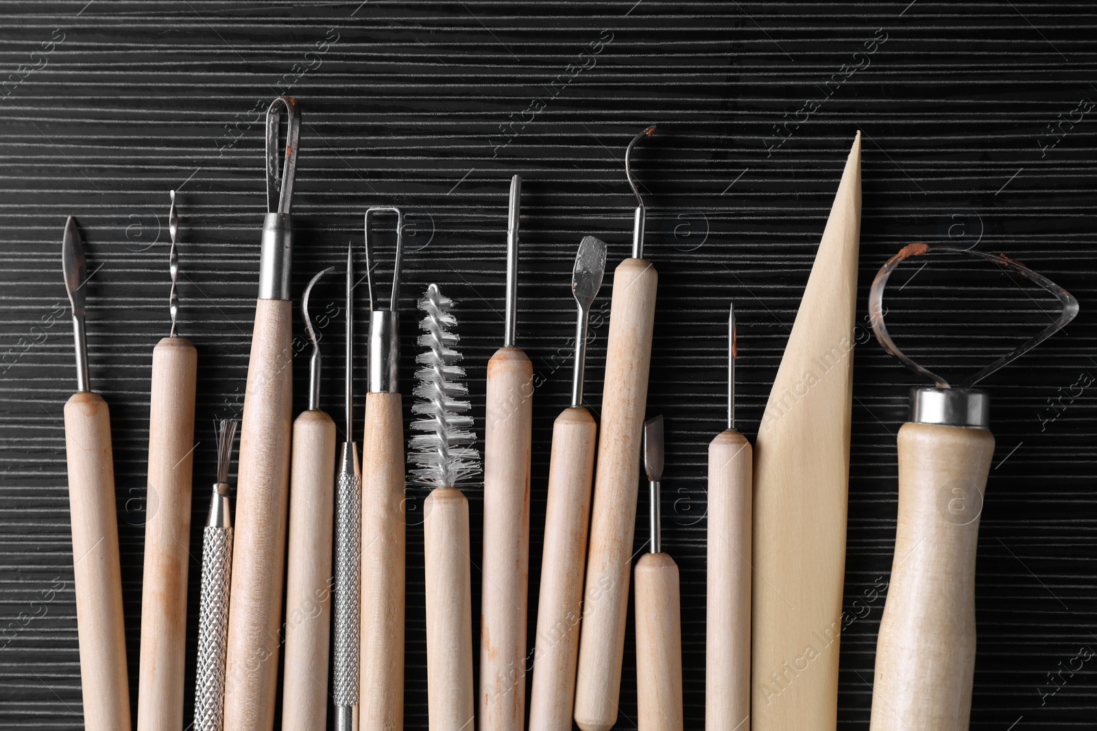 Photo of Clay and set of modeling tools on dark gray wooden table, flat lay