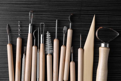 Clay and set of modeling tools on dark gray wooden table, flat lay