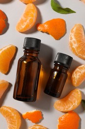 Photo of Aromatic tangerine essential oil in bottles and citrus fruit on grey table, flat lay