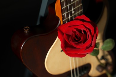 Photo of Beautiful rose near electric guitar on black background, closeup. Space for text