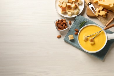 Photo of Pot of tasty cheese fondue, bread and almonds on white wooden table, flat lay. Space for text