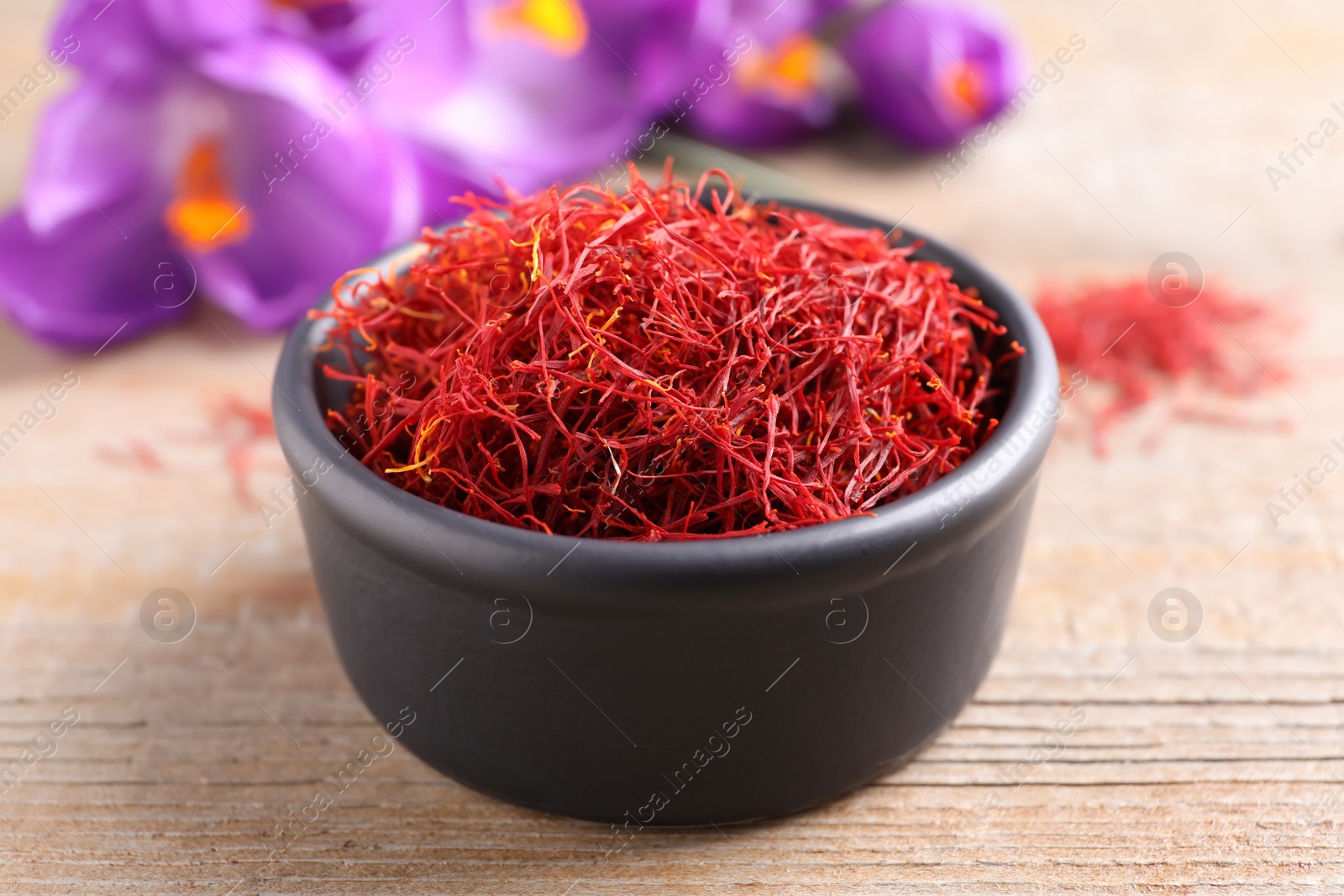 Photo of Dried saffron in bowl and crocus flowers on wooden table, closeup