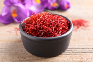 Photo of Dried saffron in bowl and crocus flowers on wooden table, closeup