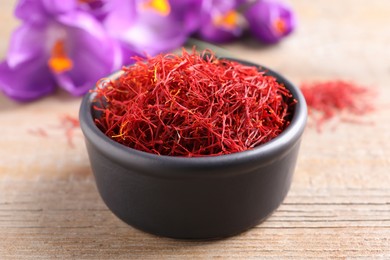 Dried saffron in bowl and crocus flowers on wooden table, closeup