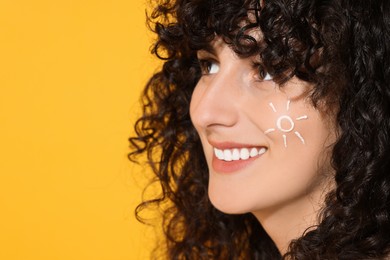 Photo of Beautiful young woman with sun protection cream on her face against orange background, closeup. Space for text