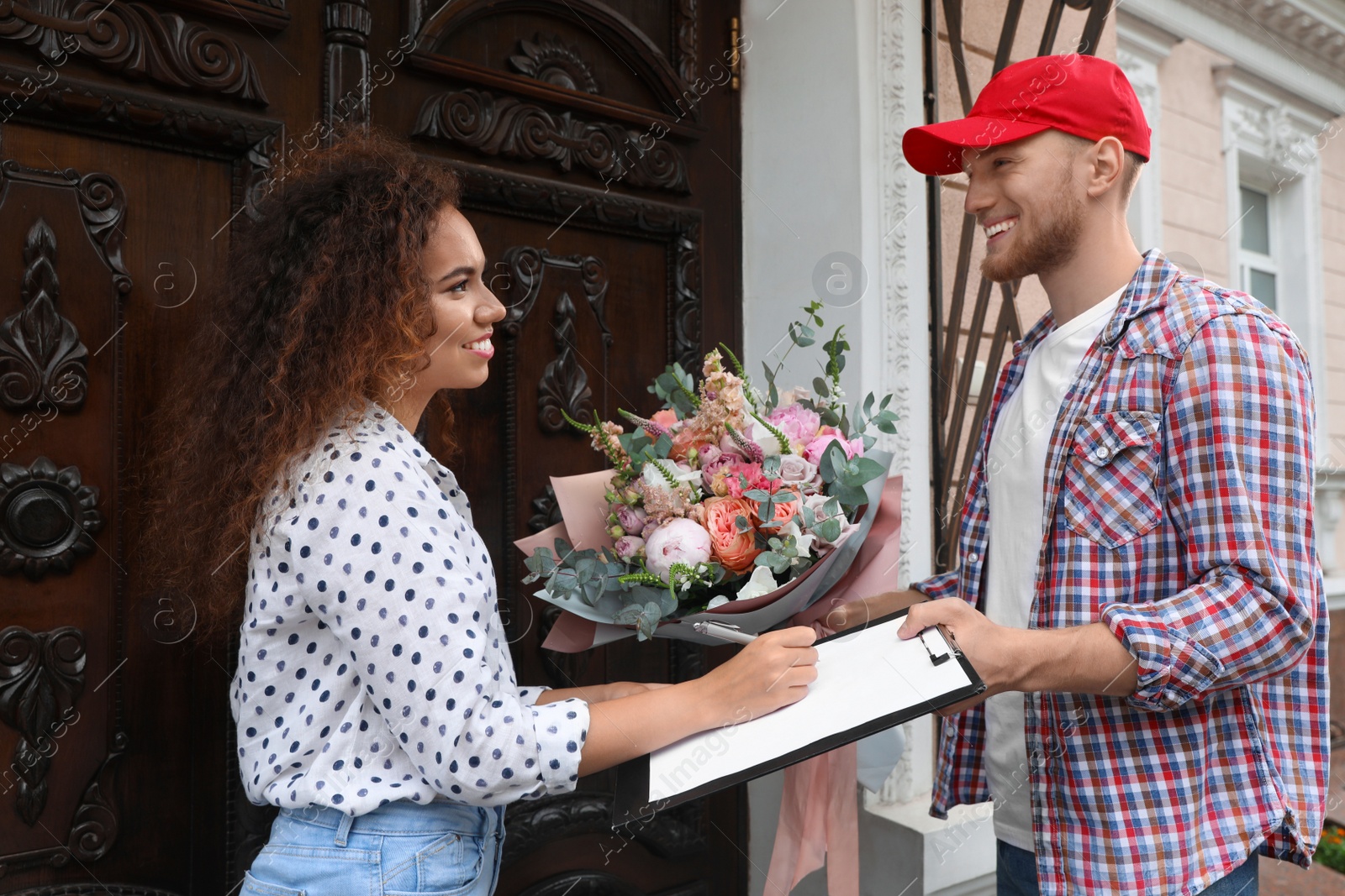 Photo of African-American woman receiving flower bouquet from delivery man at door