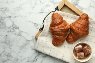 Tasty croissants served with cup of hot drink on white marble table, top view. Space for text