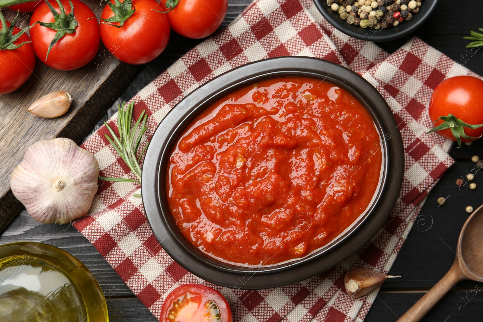 Photo of Homemade tomato sauce in bowl and fresh ingredients on black wooden table, flat lay