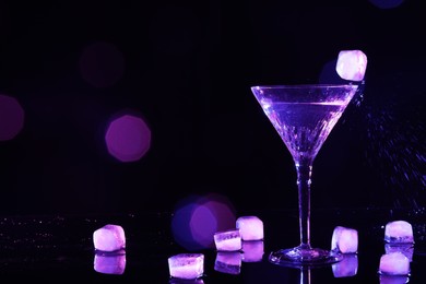 Photo of Glass of martini with ice in neon lights on dark background, bokeh effect. Space for text
