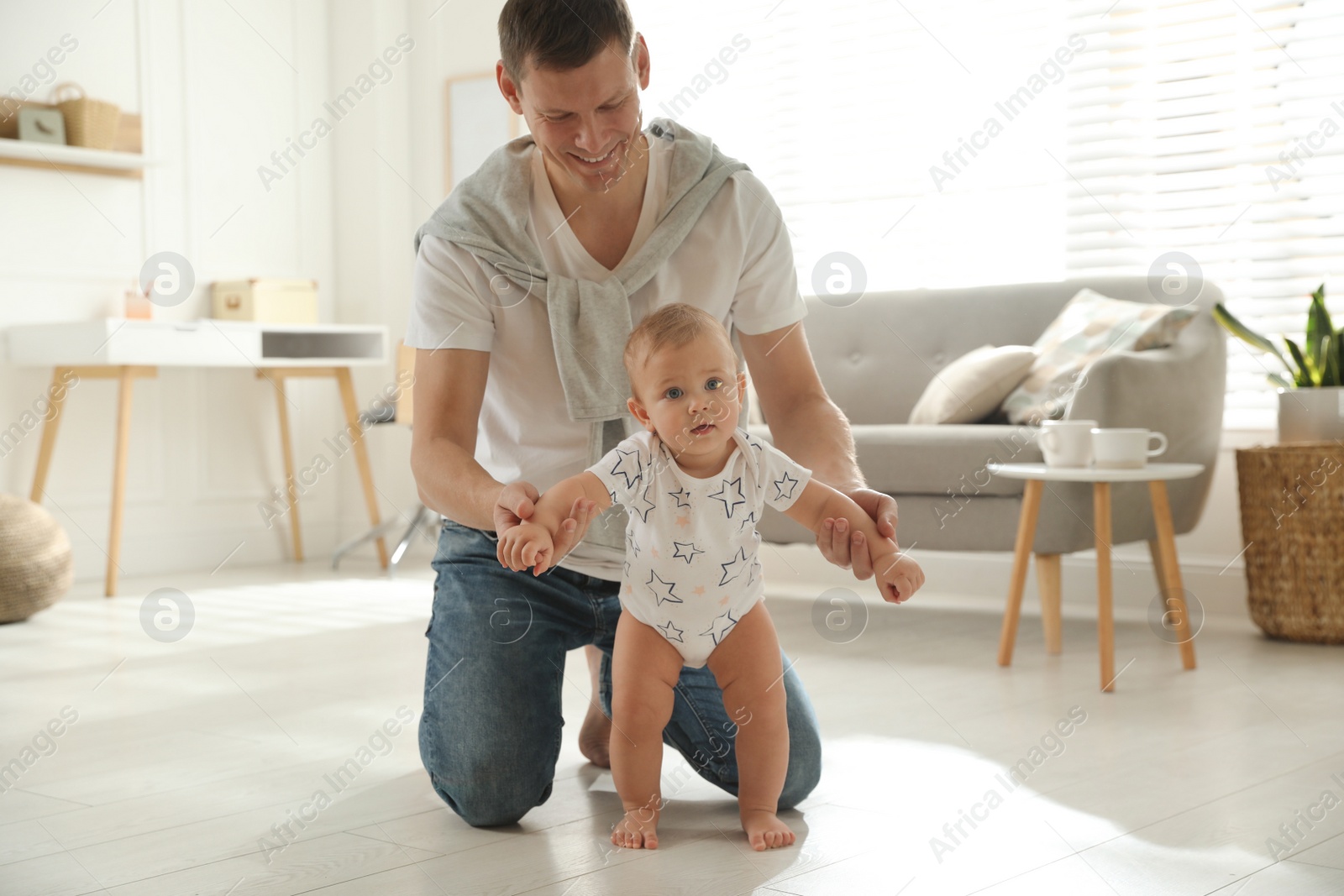 Photo of Father supporting his baby daughter while she learning to walk at home