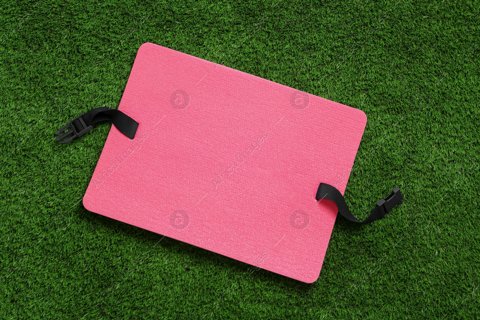 Photo of Pink foam seat mat for tourist on green grass, top view
