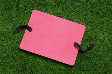 Pink foam seat mat for tourist on green grass, top view